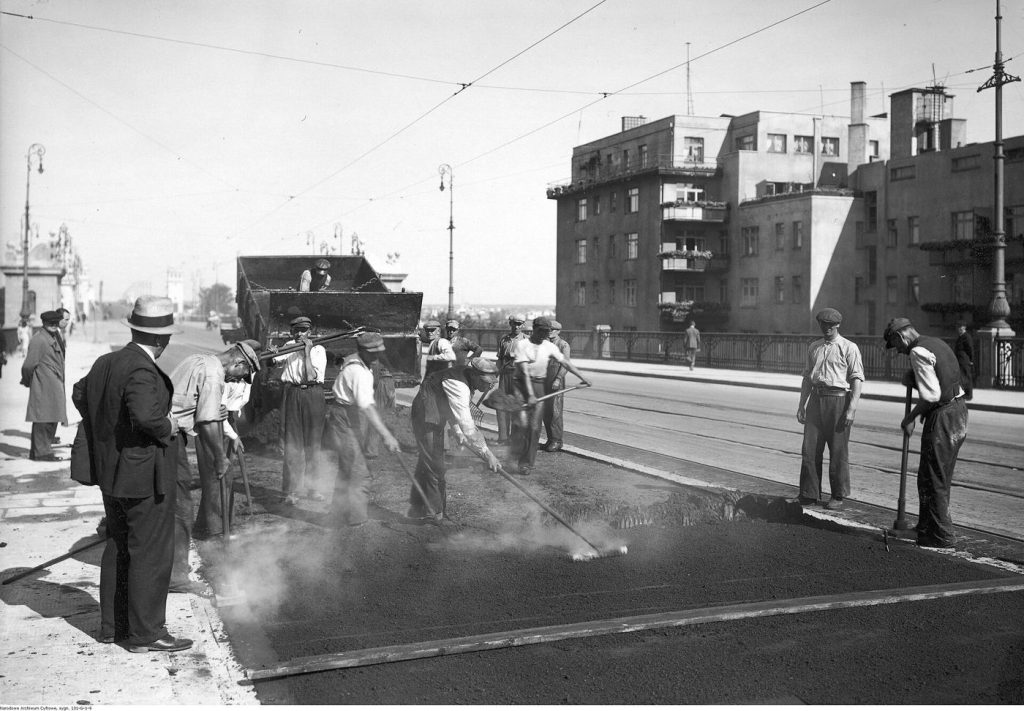 Road workers laying fresh asphalt during a road resurfacing project with machinery nearby.